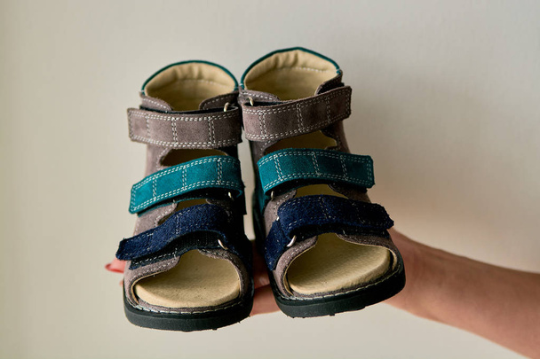 Vrouw houdt close-up een speciale kinderen orthopedische schoen sandalen gemaakt van echt leer. Comfortabele schoenen geïsoleerd op lichte achtergrond met copyspace. Beeld geschikt voor reclame. - Foto, afbeelding