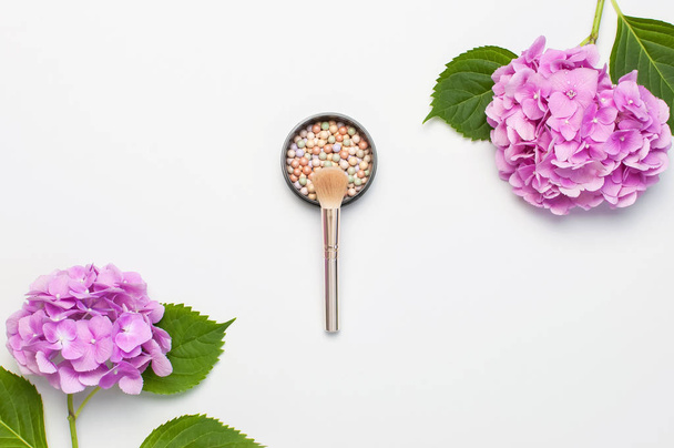 Set von dekorativen Kosmetik-Make-up-Pinseln, erröten Gesicht Kugeln, rosa Hortensien Blumen auf hellem Hintergrund Draufsicht flach legen Kopierraum. Beauty-Blogger-Konzept. Modehintergrund - Foto, Bild