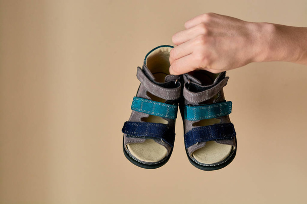 Vrouw houdt close-up een speciale kinderen orthopedische schoen sandalen gemaakt van echt leer. Comfortabele schoenen geïsoleerd op lichte achtergrond met copyspace. Beeld geschikt voor reclame. - Foto, afbeelding