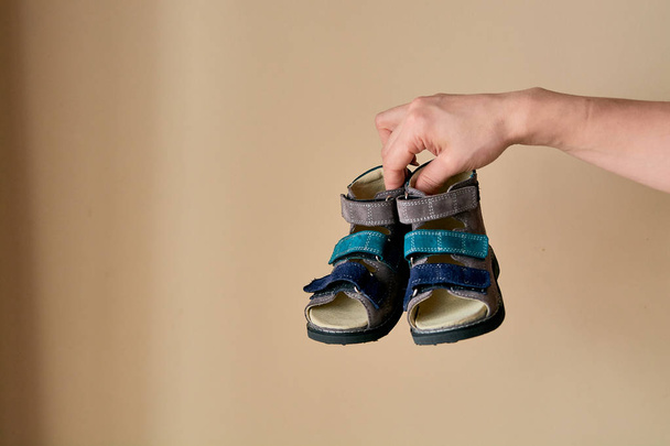 Nainen pitää lähikuva erityinen lasten ortopedinen kenkä sandaalit aitoa nahkaa. Mukavat kengät eristetty kevyellä taustalla copyspace. Mainontaan soveltuva kuva. - Valokuva, kuva