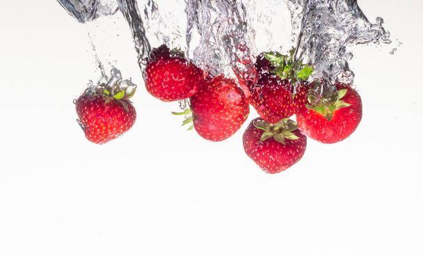 Nahaufnahme Foto, bei sehr kurzer Belichtung, Erdbeeren, die auf weißem Hintergrund ins Wasser fallen Nahaufnahme - Foto, Bild