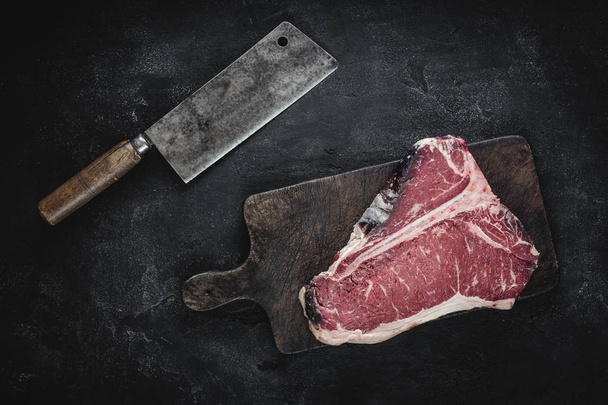 roh getrocknetes, gereiftes T-Bone-Steak auf Vintage-Schneidebrett mit Fleischspalter - Foto, Bild