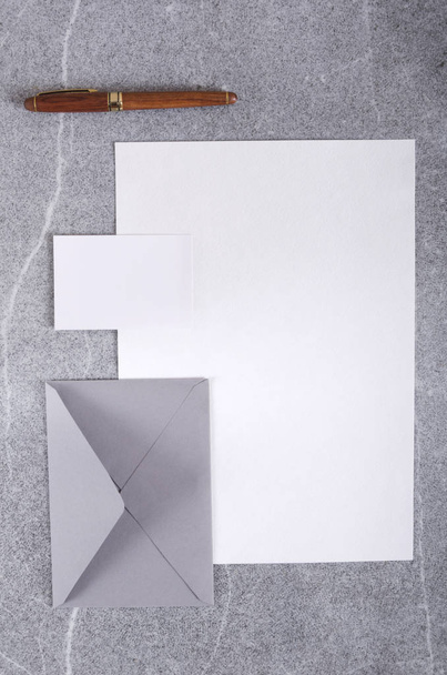 Dikey atış. Gri tablodaki boş kartvizit, zarf, kalem ve boş kağıt görünümünün üst görünümü - Fotoğraf, Görsel