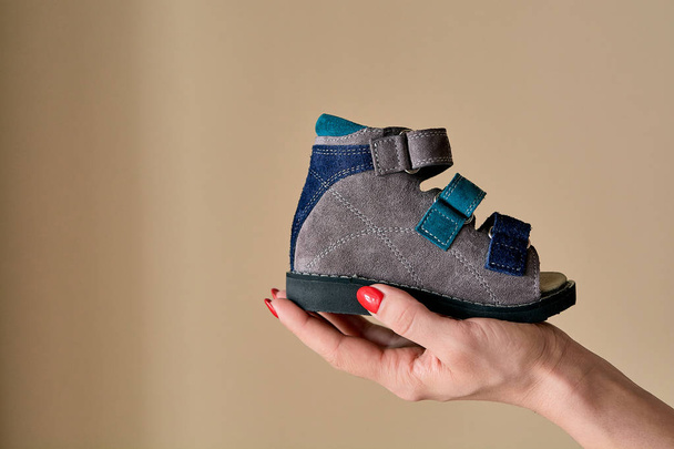 Kadın elinde hakiki deriden yapılmış ortopedik çocuk ayakkabısı sandaletleri tutuyor. Telif alanı olan hafif arka planda izole edilmiş rahat ayakkabılar. Görüntü reklam için uygun. - Fotoğraf, Görsel
