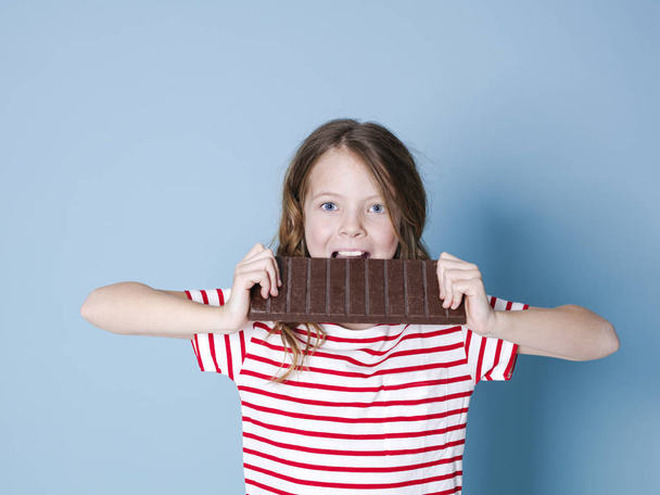 pretty blonde girl with giant bar of chocolate posing in front of blue background - Φωτογραφία, εικόνα