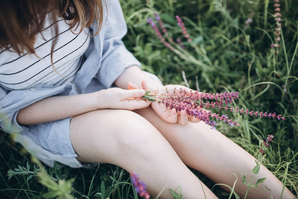 dziewczyna siedzi w zielonej trawy gospodarstwa kwiatów - Zdjęcie, obraz