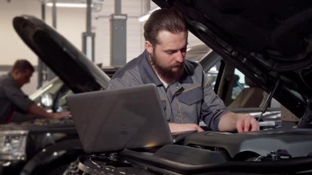 Εργαζόμενος υπηρεσία αυτοκινήτου χρησιμοποιώντας φορητό υπολογιστή, εξέταση κινητήρα του αυτοκινήτου - Πλάνα, βίντεο