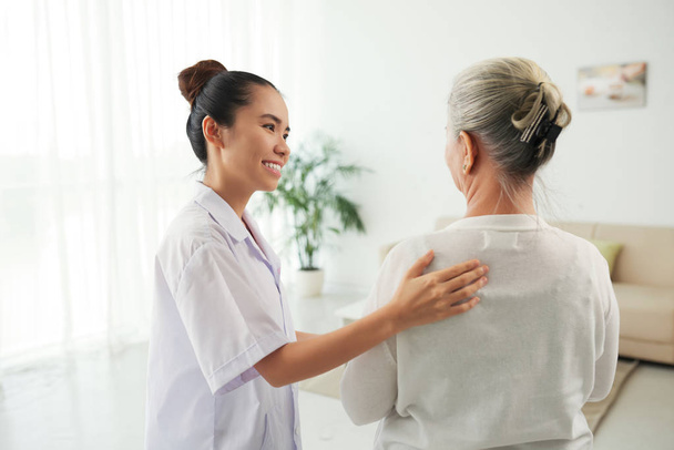 Sonriendo bonita enfermera hablando con la mujer mayor en casa
 - Foto, imagen