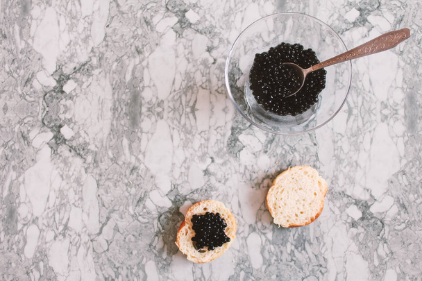 Vista superior de sanduíche saboroso com caviar preto sobre fundo de mármore branco. .Espaço livre para texto. Caviar preto. Delícia culinária luxuosa
. - Foto, Imagem