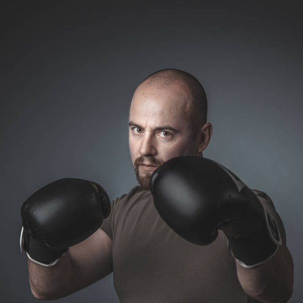 adult man with casual clothes and boxing gloves, looks directly  - Фото, изображение