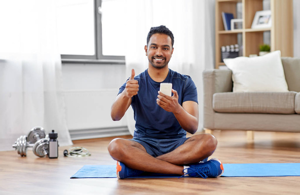 indian man with smartphone on exercise mat at home - Foto, imagen