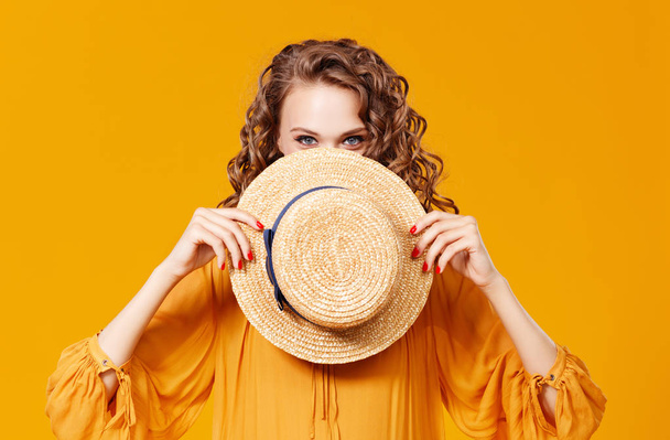 schöne junge lockige Frau mit Sommermütze auf gelbem Hintergrund - Foto, Bild