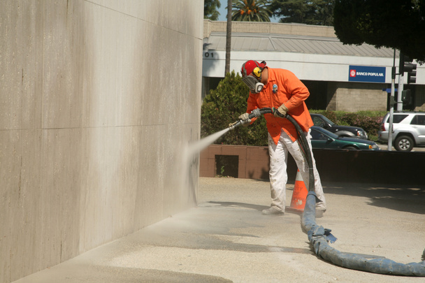 An unidentifiable city worker sand blast away graffiti on a wall - Photo, Image