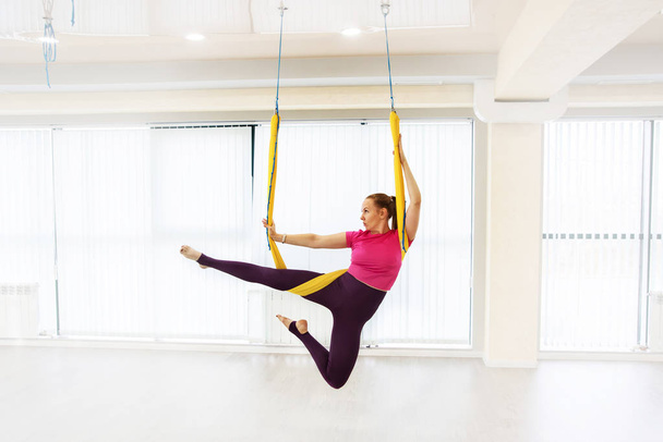 Fit hübsche junge Frau trägt Sportbekleidung dabei fliegen Yoga Stretching-Übungen in Fitness-Training weißen Turnhalle Loft Klassenzimmer. - Foto, Bild