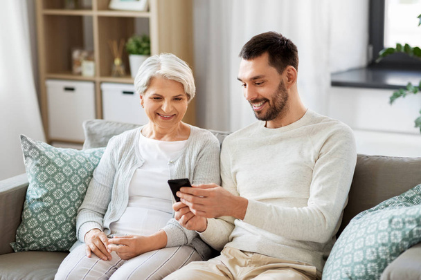 old mother and adult son with smartphone at home - Valokuva, kuva