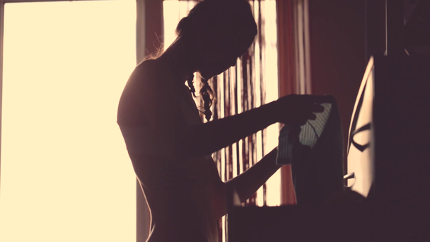 jonge slanke aantrekkelijke vrouw in ondergoed en jeans ziet en probeert op kleding van de dressoir in de slaapkamer. silhouet van mooie sexy jonge vrouw thuis tegen raam. - Video