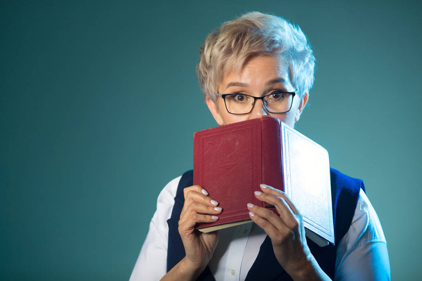 stylish elderly woman in glasses with a book in her hands with a surprised face - Фото, изображение