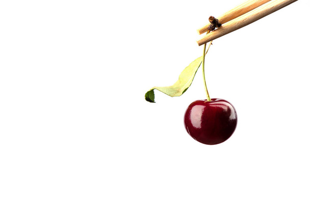 Chopsticks with ripe cherries over white background. - Foto, afbeelding