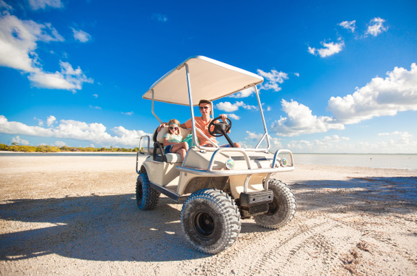 vader met zijn twee dochters golfkar rijden op tropisch strand - Foto, afbeelding