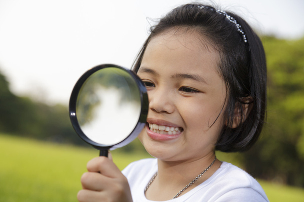 Asian little girl holding a magnifying glass in outdoor - Фото, изображение