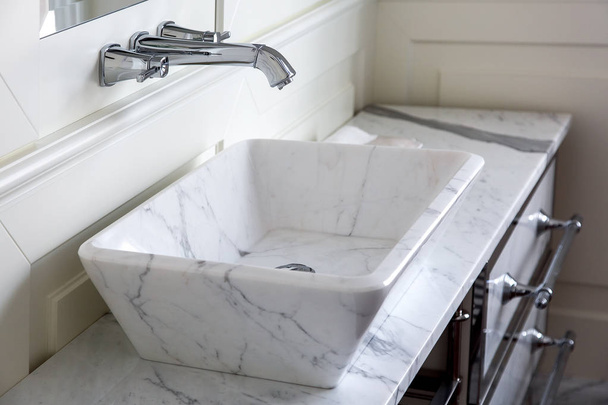 Chrome-plated faucet with white marble washbasin and worktop in the bathroom with wood panel walls, close up details
. - Фото, изображение