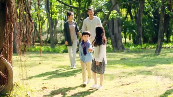 Azjatycka rodzina z dwójką dzieci relaksujący spacer w parku - Materiał filmowy, wideo