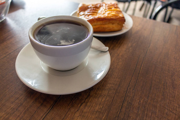 xícara de café servida em uma mesa ao lado de um bolo de abacaxi
 - Foto, Imagem