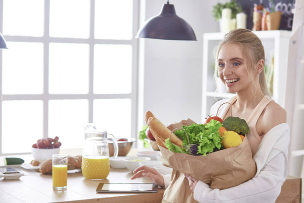 Nuori nainen tilalla ruokakauppa laukku vihanneksia Seisoo keittiössä - Valokuva, kuva