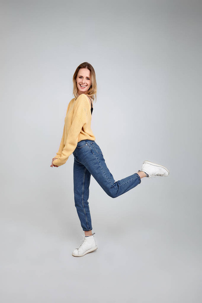 Feeling comfortable in her style. Full length studio shot of attractive young woman in casual wear smiling and looking away while jumping against grey background - 写真・画像