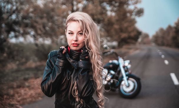 Stylish biker woman with motorcycle on the road. - Zdjęcie, obraz