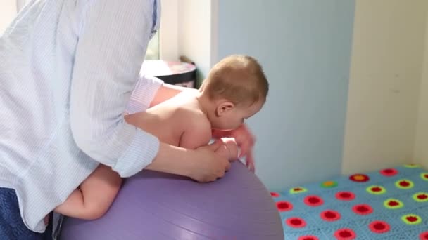 Mom does exercises for development with the baby on the fitball. Baby development concept, caring mom, toning exercises for babies - Video