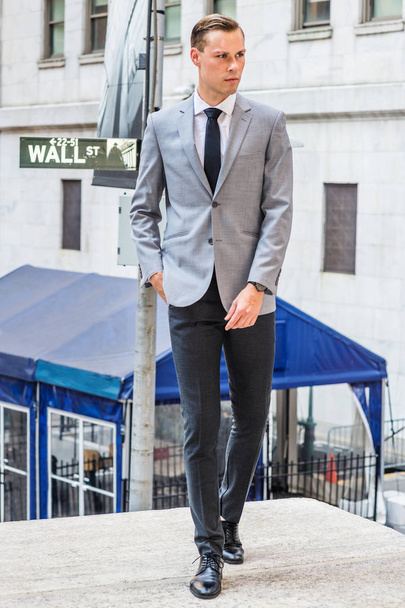 Young Businessman Street Fashion à New York. Homme vêtu d'un blazer gris, chemise blanche, cravate noire, pantalon, chaussures en cuir, debout dans la rue à l'extérieur du bureau par panneau Wall Street, impatient
 - Photo, image