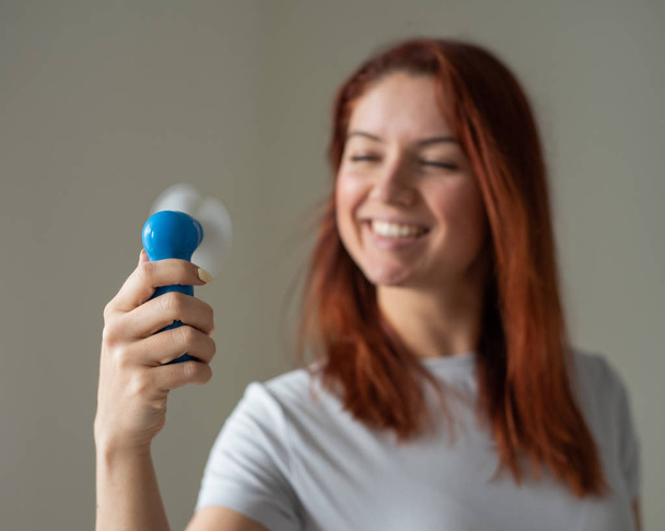 Portrait of a red-haired smiling woman with a pocket fan in her hands. Full face of a girl refreshing in the heat of a wind blow from a wireless electric device. Cool air flow from the air conditioner - Zdjęcie, obraz