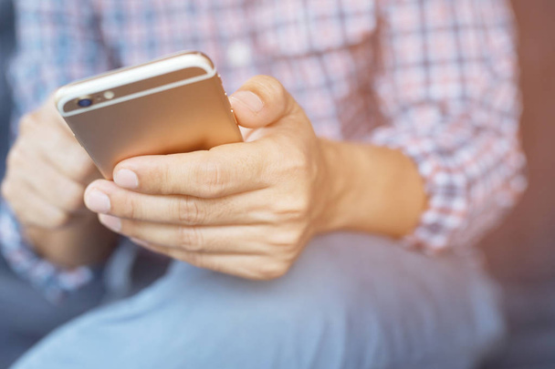 Молодой бизнесмен в клетчатой рубашке пользуется мобильным телефоном во время отдыха в офисе. сидя диван в просмотре сообщения на мобильном телефоне во время перерыва
. - Фото, изображение