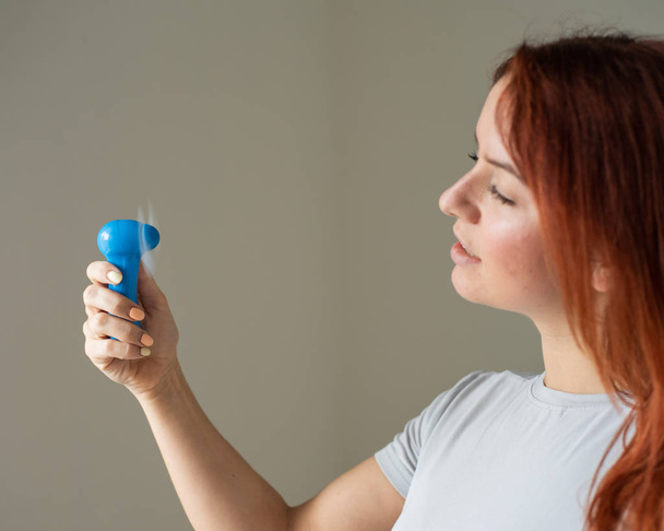 Portrait of a red-haired woman with a pocket fan in her hands. Profile of a girl refreshed in the heat by a wind blown from a wireless electric device. Enjoy the cool airflow from the air conditioner. - Foto, Bild