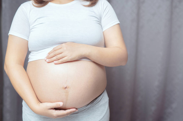 Nieuwe moeder zwangere vrouw in wit ondergoed gebruik hand aanraking buik buik met baby. Jonge vrouw verwacht een baby staan in de buitenlucht. - Foto, afbeelding