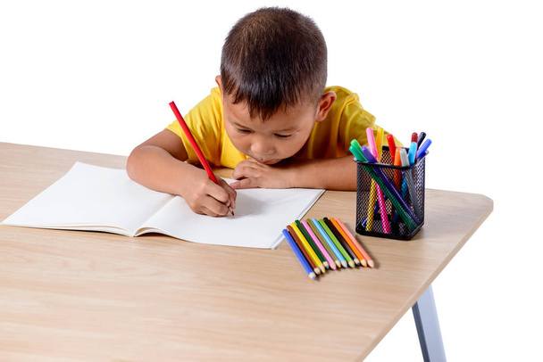 Cute cheerful child drawing using color pencil while sitting at  - Photo, image