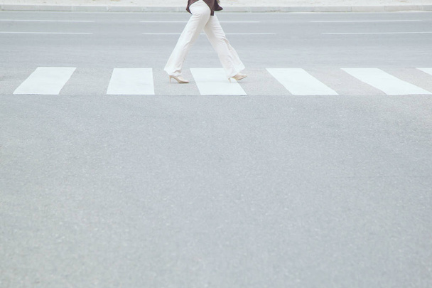 Joven mujer de negocios estilo mujer trabajadora con zapatos casuales de tacón alto caminando a través del paso de peatones en la calle de cruce de la ciudad, concepto de seguridad peatonal, espacio vacío, escribir un mensaje en la carretera
. - Foto, imagen