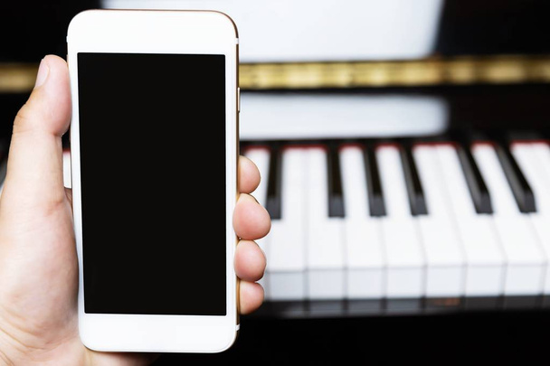 close up de pessoas mão segurando telefone inteligente móvel branco com tela vazia em branco. inserir Escreva uma mensagem ou Aplicação. piano teclado fundo
. - Foto, Imagem