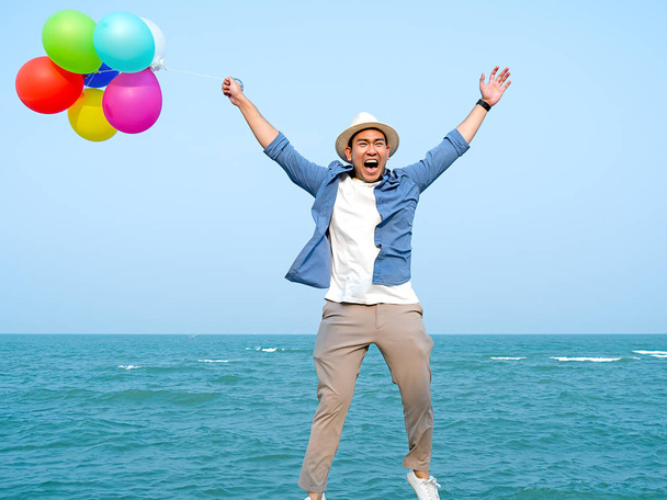 Heureux homme asiatique tenant des ballons colorés et sautant contre bl
 - Photo, image