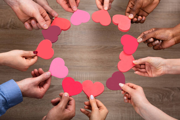 High Angle View Of People's Hand Making Circular Shape With Hearts Against Wooden Background - Foto, Imagem