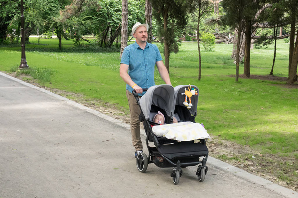 Ojciec z dziećmi w podwójnym wózku w parku. Mężczyzna pchanie bliźniaki wózek, wózek.  - Zdjęcie, obraz