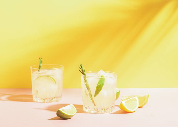 ein Getränk aus Zitrone und Limette in eleganten Gläsern pastellfarbenen Hintergrund mit strahlendem Sonnenschein. Sommer-Limonade oder Mojito. - Foto, Bild