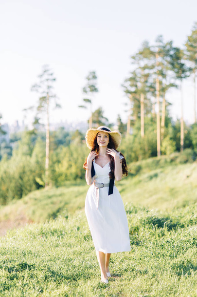  Όμορφο κορίτσι με λευκό φόρεμα και καπέλο. Καλοκαιρινή φωτογράφηση στο πάρκο στο ηλιοβασίλεμα. - Φωτογραφία, εικόνα
