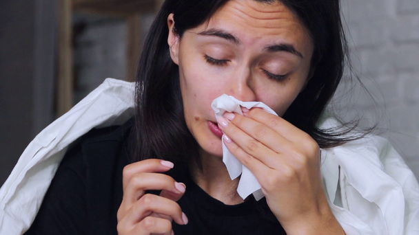 A young woman sitting at home on the bed, sick, blowing his nose in a handkerchief - Imágenes, Vídeo