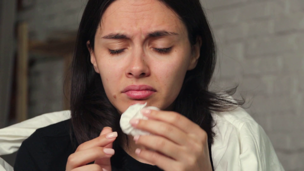 Egy fiatal nő ül otthon az ágyon, beteg, fújja az orrát a zsebkendőjét - Felvétel, videó