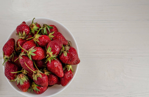 Fresh summer ripe strawberries in a white plate on a white woode - Fotó, kép