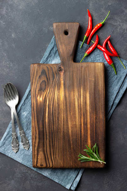 Food cooking concept. Vintage wooden kitchen board, cutlery and red pepper over napkin on dark stone background. Top view. - Photo, image
