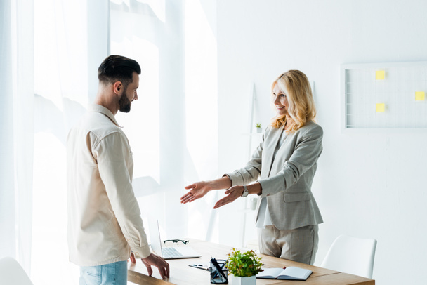 happy blonde recruiter gesturing in office near handsome bearded man  - Photo, Image