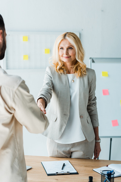 selective focus of blonde recruiter shaking hands with employee in office  - Photo, Image